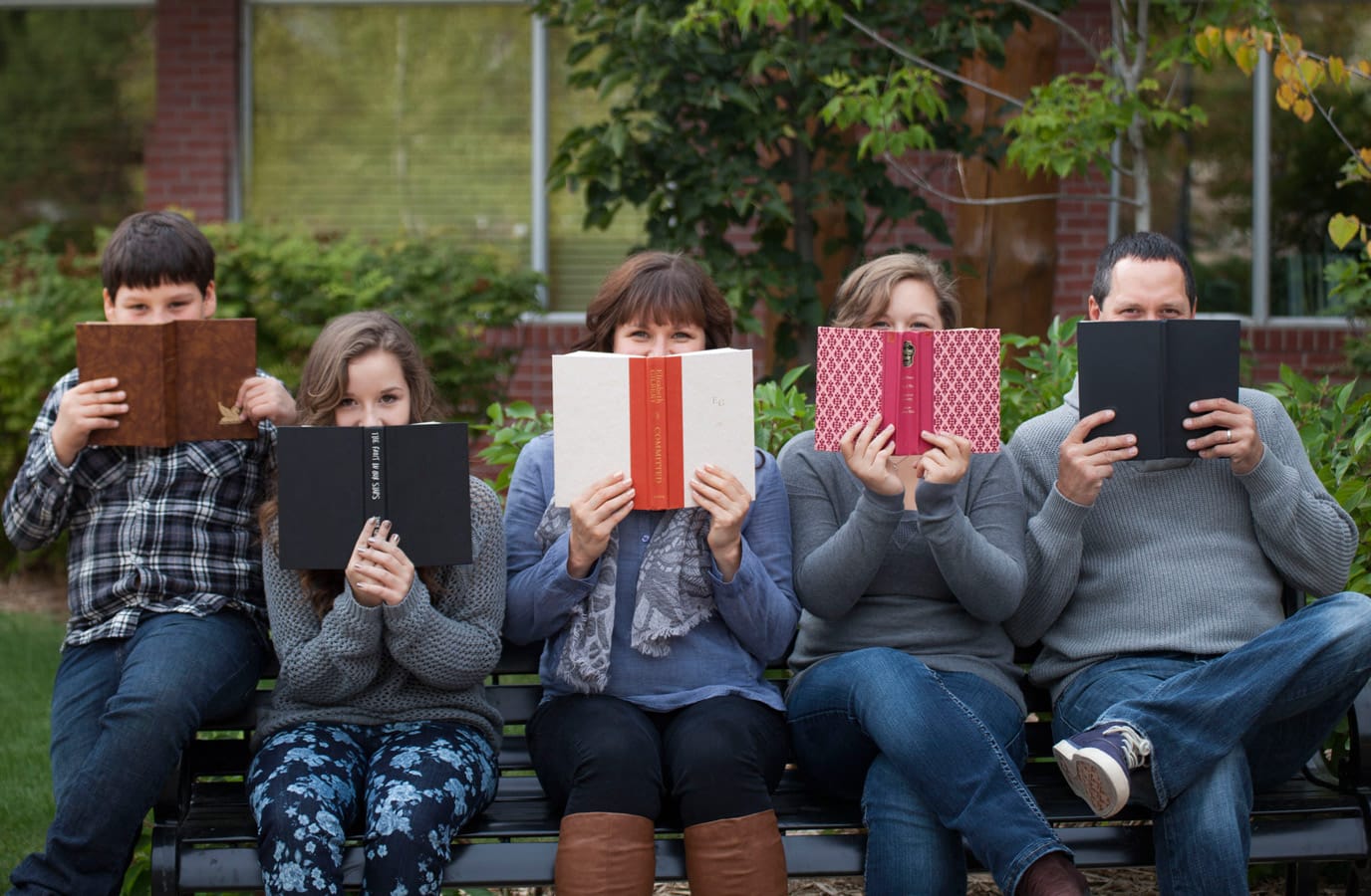a family smiles behind books during a portrait session in Prince Albert