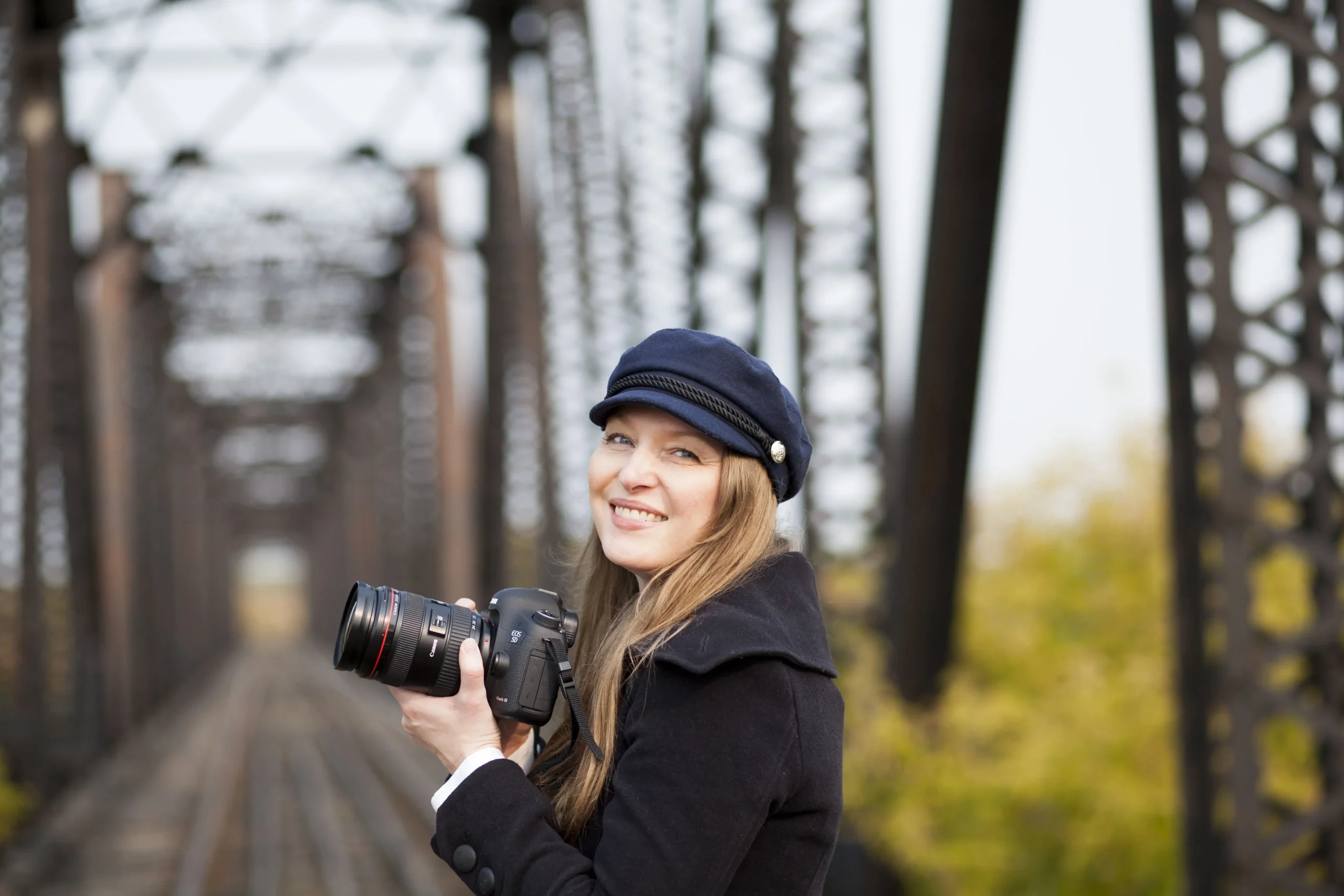 Prince Albert photographer Tamera North of UBU Photos, holding a camera smiling on a city bridge